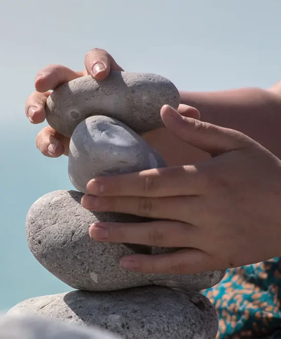 Balanced Stones Beside the Water Stacked stones and a hand holding a stone beside calm blue water