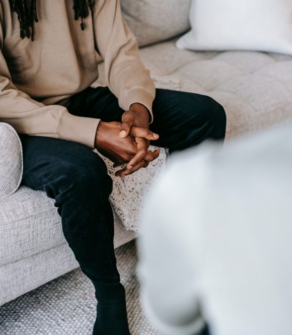 Therapy Conversation on a Sofa Person sitting on a sofa with hands clasped during a conversation